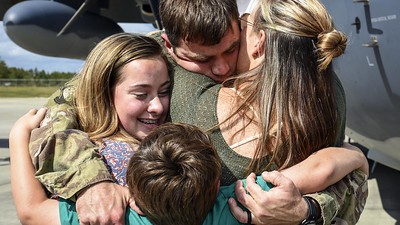 A man, woman, teenager and child hug in a warm family embrace